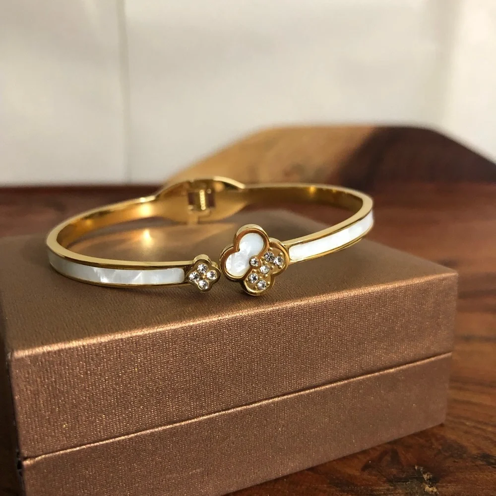 gold-toned hinged bangle bracelet featuring white clover motifs and crystal New